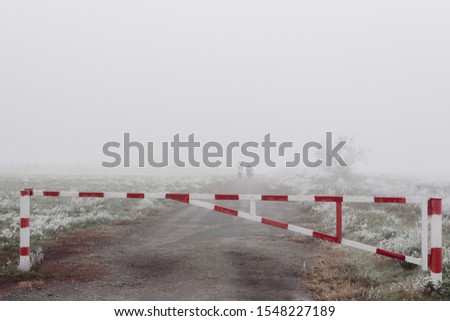 Red and white road barrier on foggy autumn day and poorly distinguishable silhouettes of two people