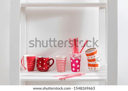 Different red mugs and glasses stand on a shelf in the kitchen