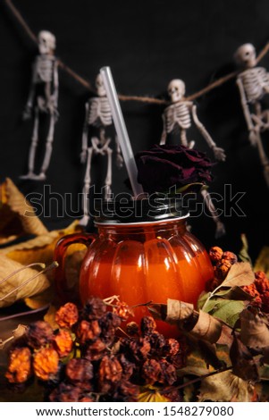  glass in the shape of a pumpkin on a background of skeletons and dry leaves                