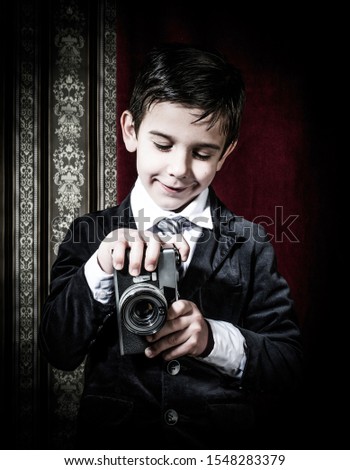 Boy with vintage camera. Vintage clothes. Kid photographer on gothic ornamental wallpaper background. Taking pictures with old camera.