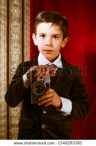 Boy with vintage camera. Vintage clothes. Kid photographer on gothic ornamental wallpaper background. Taking pictures with old camera.