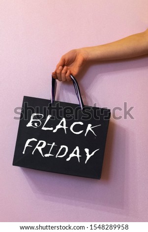 black gift shopping bag with Black Friday sale, holds in hand on pink background.
