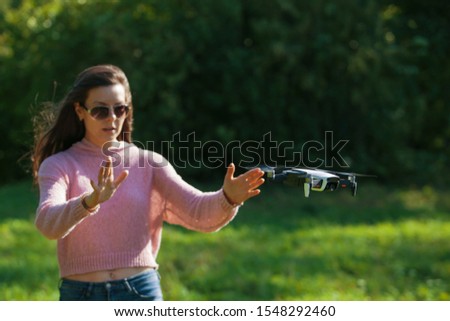 Walk with a drone. A young woman in black glasses launches a low flying drone. Reaches out to a low flying drone, gesture control. Blurred background. Front view.