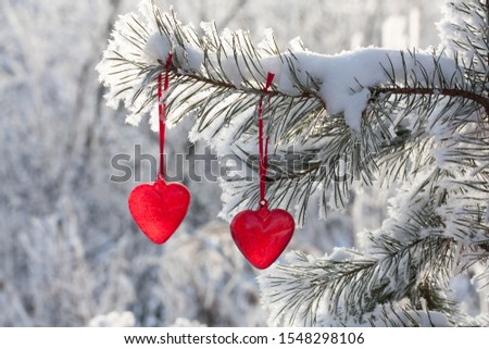 Two read hearts hanging on a snow-covered pine tree, vintage glass Christmas decoration