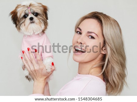 beautiful cute girl holding a well groomed shih tzu puppy in a pink sweater