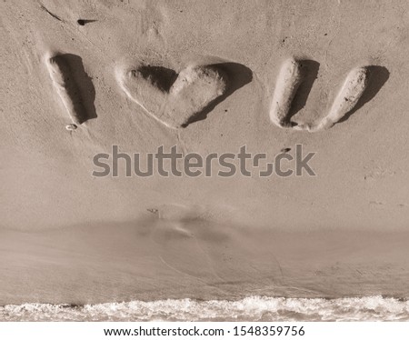 Phrase "I love you" made of sand. Bulky sandy letters and sea wave. Black and white. Upside down view.
