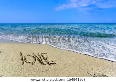 LOVE, creative abstract graphic message for your summer design. Inscription on wet sand word LOVE drawn on the sand of a beach at ocean horizon. Concept photo of summer vacation.