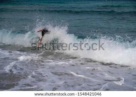 Young man riding a wave on a skimboard (a mix of surf and skate) in Cala Mesquida (Mallorca, Spain) consists of running from the shore, dropping on the board, sliding to a wave and catching it.