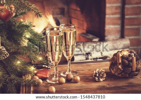 Christmas composition - Two glasses with champagne on a wooden table near a Christmas tree in a room with a burning fireplace.