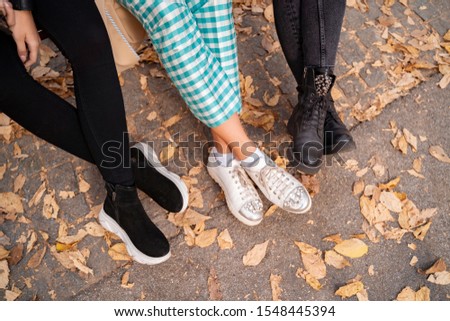 Closeup shot of legs of trendy females, dry leaves on the ground, fall-winter shoe collection concept 