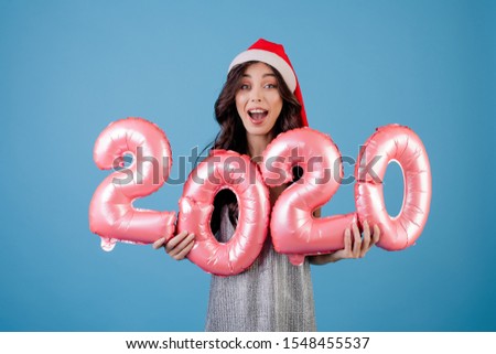 woman holding 2020 new year balloons wearing santa hat and dress