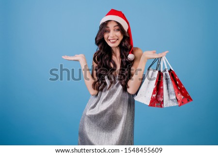woman with presents in shopping bags wearing santa hat isolated over blue
