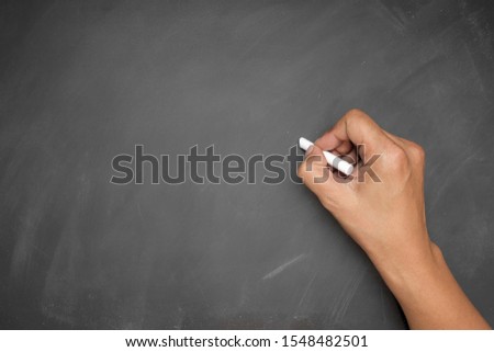 The man hand holding white chalk writing on blackboard or chalkboard