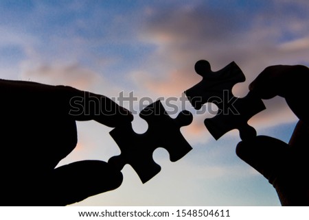 Hand hold jigsaw puzzle with silhouette sunlight effect sky clouds.
Strategies for business success. 
Collaboration and teamwork concept.
 