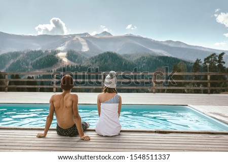 Two teen friends spending winter or spring vacation in luxury spa resort with swimming pool over alpine mountain landscape