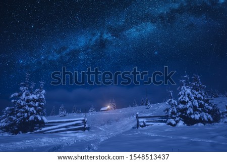 Bright milky way in a night starry sky. Lonely house on a snowy hill with Christmas light.