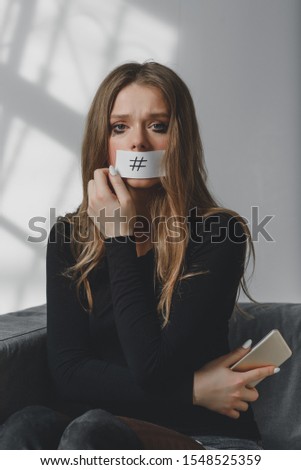 Portrait of a young beautiful sad girl, whose mouth is sealed with a hashtag, as a symbol of the influence of the social network on the mental health of a person.