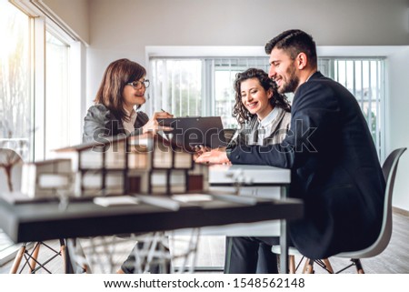 Side view image of young happy family sitting in consulting office, making property purchase. Mature realtor helping business couple do financial investment. Installment payment, mortgage loan concept Royalty-Free Stock Photo #1548562148