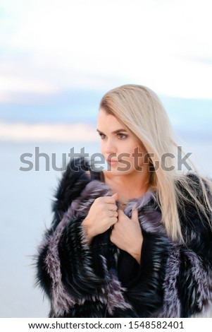 Caucasian blonde woman wearing black transparent dress standing on snowed background. Concept of winter photo session an fashion.