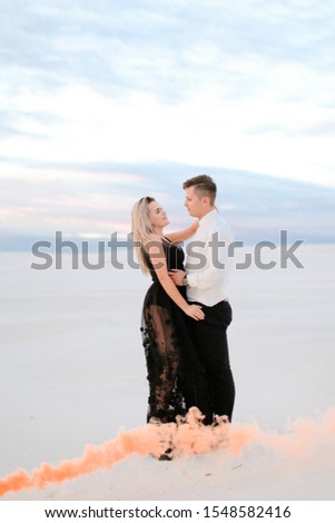 Young caucasian girl wearing transparent black dress hugging man in snowed steppe. Concept of winter photo session and love.