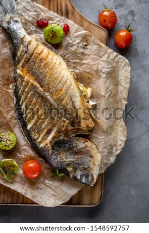 Grilled dorado fish with vegetables. Fried fish food picture on a dark background.