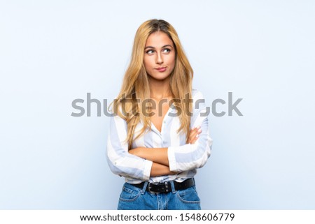 Young blonde woman over isolated blue background with confuse face expression