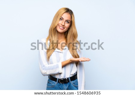 Young blonde woman over isolated blue background presenting an idea while looking smiling towards