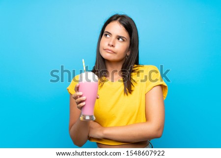 Young girl with strawberry milkshake over isolated background making doubts gesture while lifting the shoulders