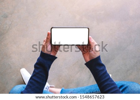 Top view mockup image of a woman holding black mobile phone with blank white screen while sitting on the floor