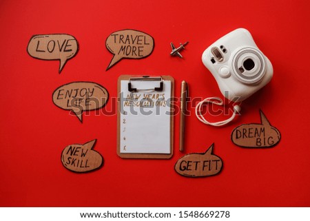 New years resolutions, photo camera, plane, clipboard on the red background. Motivations and plans for the New year. 