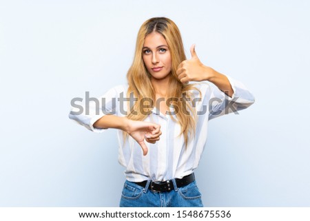 Young blonde woman over isolated blue background making good-bad sign. Undecided between yes or not