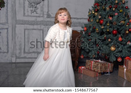 a girl in a white dress and a fur coat is spinning in a white dress in the hall with a Christmas tree