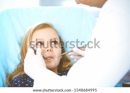 Little baby girl sitting at dental chair with open mouth during oral check up while doctor. Visiting dentist office. Medicine concept. Toned photo