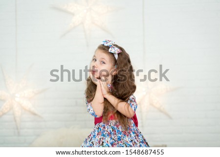 Cute little girl in a beautiful dress presses her hands to her face in surprise.