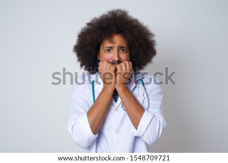 Anxiety. beautiful young African American doctor man covering his mouth with her hands and standing indoors. Scared from something or someone bitting nails.