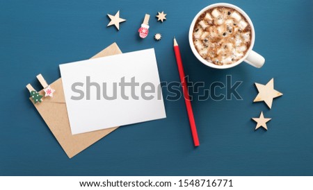 Letter to Santa Claus mockup. Flat lay blank paper card, craft envelope, red pencil, coffee cup with marshmallows, wooden decorations on blue background. Top view. Christmas letter concept.