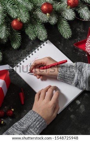 Write a letter to Santa hand on a festive decorated table. Christmas composition. Dark background