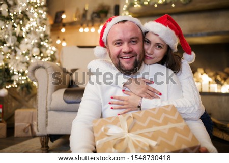Picture of man and woman in Santa's caps sitting on floor with gifts.