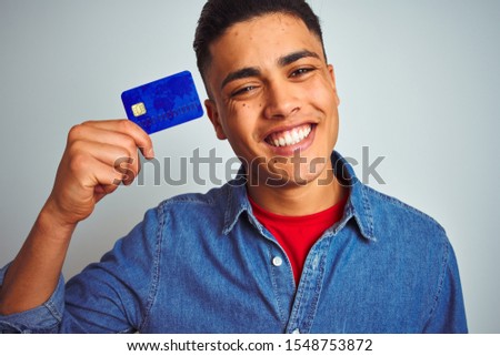 Young brazilian customer man holding credit card standing over isolated white background with a happy face standing and smiling with a confident smile showing teeth