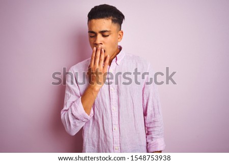 Young brazilian man wearing shirt standing over isolated pink background bored yawning tired covering mouth with hand. Restless and sleepiness.