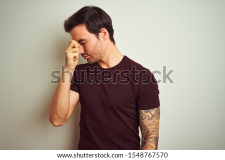 Young handsome man with tattoo wearing purple casual t-shirt over isolated white background tired rubbing nose and eyes feeling fatigue and headache. Stress and frustration concept.