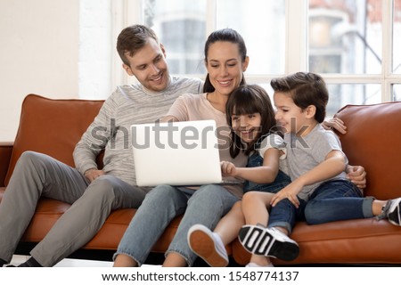 Happy young family with cute preschooler kids have fun at home watching movie on laptop together, loving parents and little children relax in living room smile enjoying cartoon on computer
