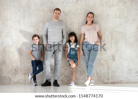 Portrait of young happy family with little preschooler kids stand near wall looking at camera smiling, middle-aged parents enjoy time with small children posing together in modern new home
