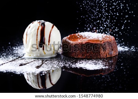 Warm dessert chocolate cake Fondant served on plate with ice-cream ball, cacao, icing sugar is pouring. Chocolate lava cake Molten on Dark black background