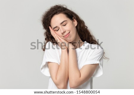 Calm happy young female in white t-shirt isolated on grey studio background relax take nap with head on hands, smiling peaceful millennial girl sleep peacefully see dreams, rest after hard day