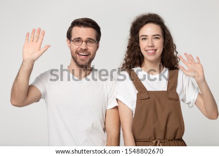 Happy millennial couple isolated on grey studio background wave talking on video call using fast internet provider, smiling man and woman greeting having web conversation via wireless connection