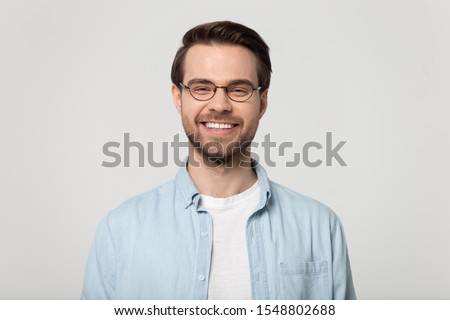 Happy millennial Caucasian guy wear glasses isolated on grey studio background smiling with white healthy teeth, positive young man in casual clothes posing look at camera show good treatment result