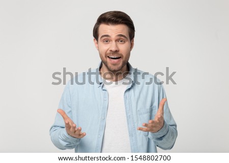 Shocked young man in blue casual shirt isolated on grey studio background look at camera talking or telling news, surprised millennial guy make hand gesture announce good sale offer or discount Royalty-Free Stock Photo #1548802700