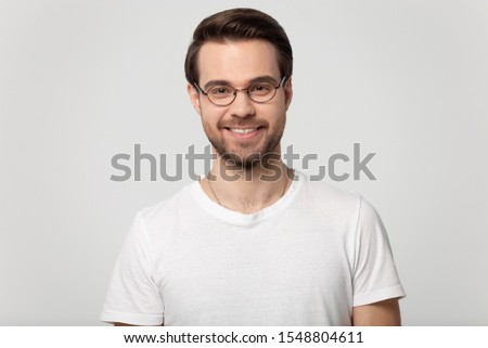 Headshot portrait of smiling millennial man in glasses and white t-shirt isolated on grey studio background look at camera, happy young male student freelancer wear spectacles posing indoors
