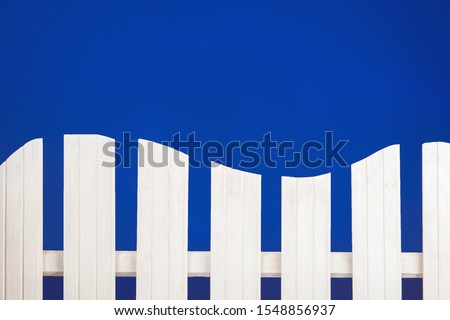 Tree fence. White fence on a blue background. Background for children. Fence in a rustic style. Paling in the form of a sea wave. Rustic palisade of white color. Place for an inscription over paling.